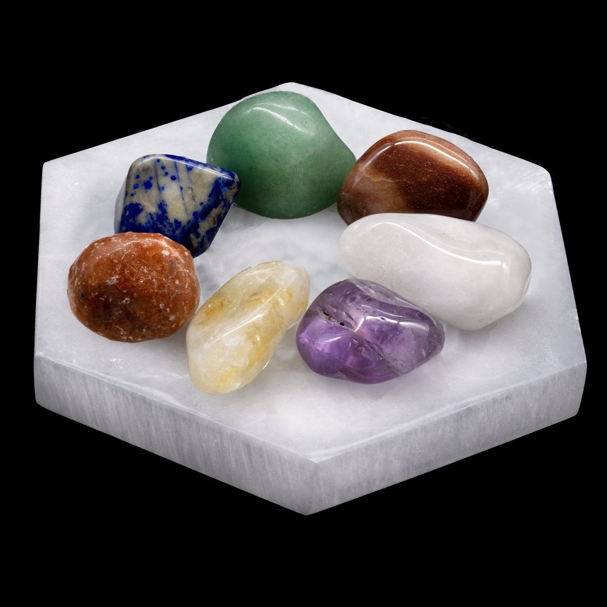 Seven colorful tumbled gemstones on a white selenite hexagon plate, with a black background.