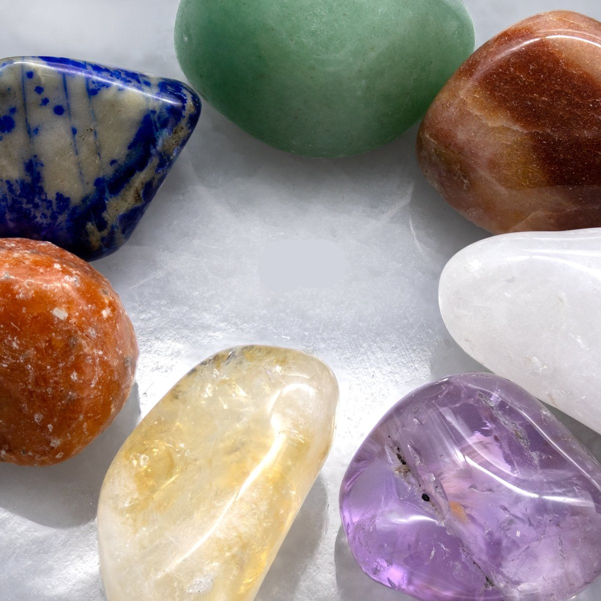 Seven colorful tumbled gemstones on a white selenite hexagon plate.