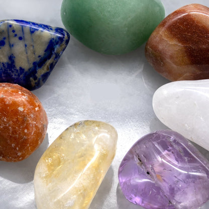Seven colorful tumbled gemstones on a white selenite hexagon plate.