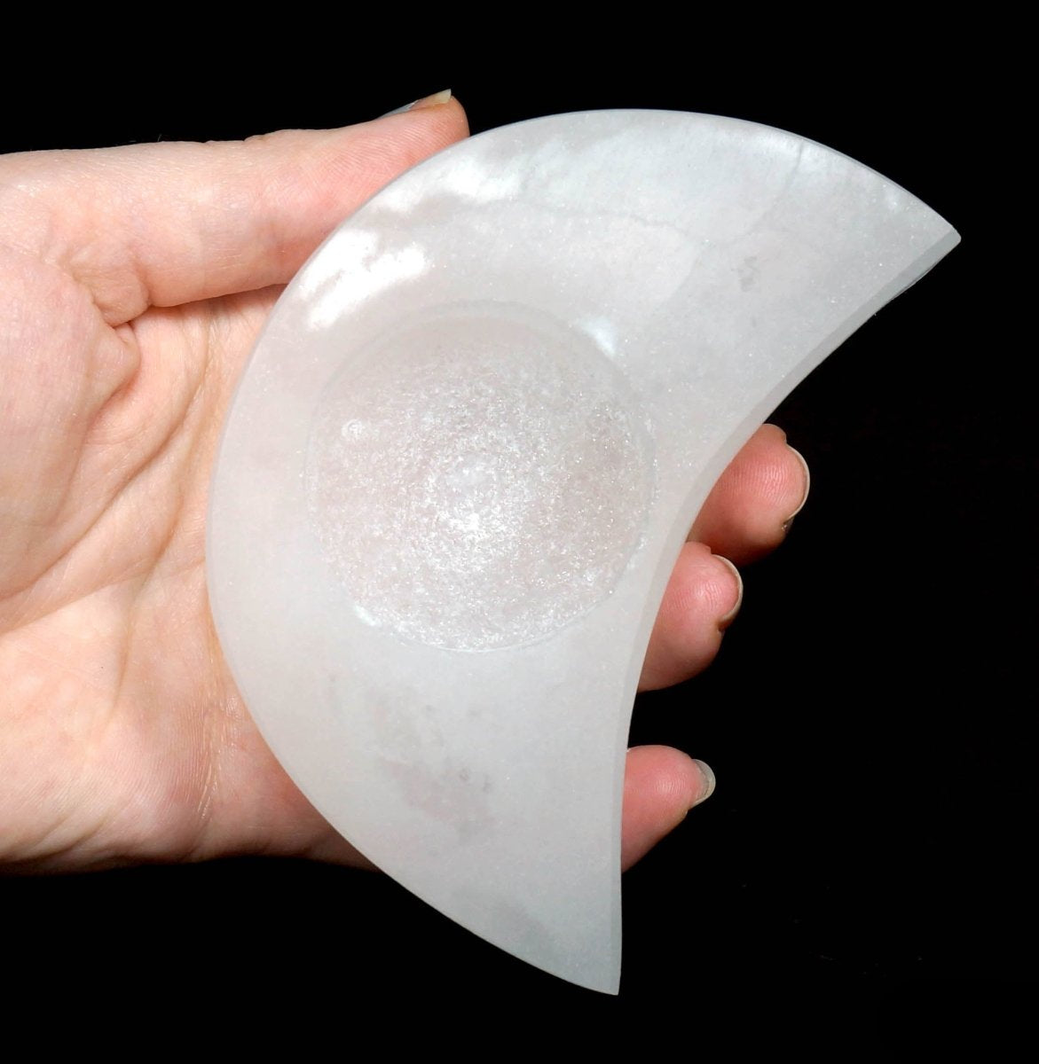 Selenite Moon Tealight being held on a black background.